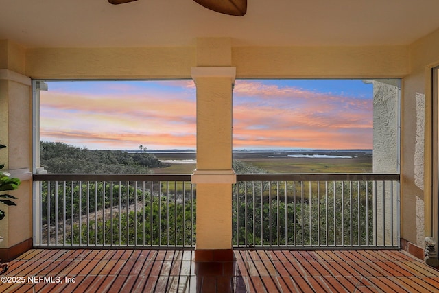 balcony at dusk with a water view and ceiling fan