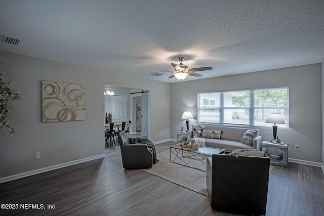 living room featuring dark wood-type flooring, ceiling fan, a barn door, and a textured ceiling