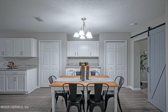 dining area featuring dark hardwood / wood-style flooring, a barn door, a chandelier, and a textured ceiling