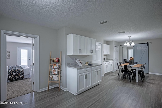 kitchen with a barn door, dark hardwood / wood-style floors, hanging light fixtures, and white cabinets