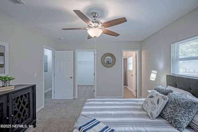 carpeted bedroom featuring ceiling fan, a walk in closet, connected bathroom, and a textured ceiling