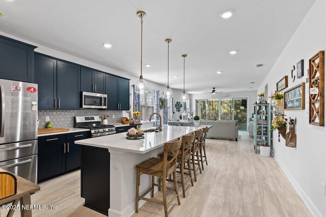 kitchen with pendant lighting, a breakfast bar area, a kitchen island with sink, backsplash, and stainless steel appliances