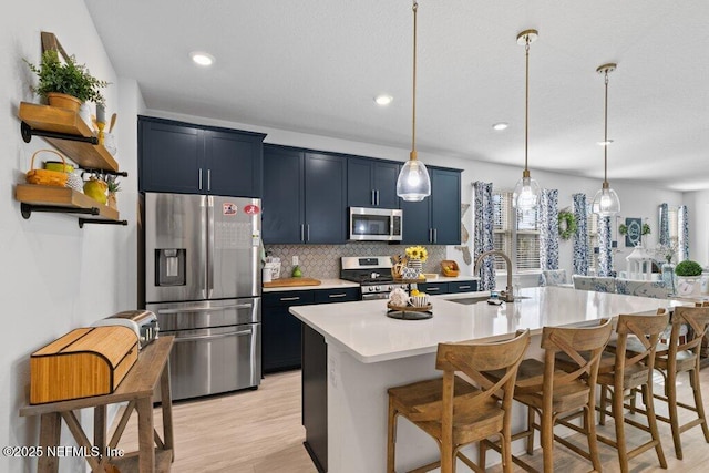 kitchen with pendant lighting, a kitchen bar, stainless steel appliances, blue cabinetry, and a center island with sink