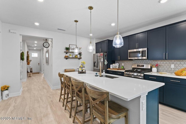 kitchen featuring appliances with stainless steel finishes, pendant lighting, backsplash, a kitchen bar, and a center island with sink