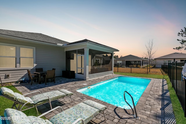 pool at dusk with a sunroom and a patio area