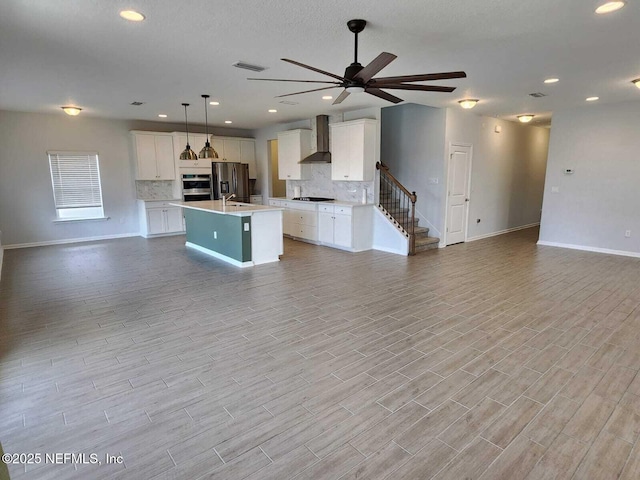 kitchen featuring decorative light fixtures, a center island with sink, white cabinets, and wall chimney exhaust hood