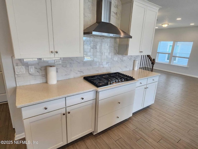 kitchen featuring white cabinetry, backsplash, stainless steel gas cooktop, and wall chimney range hood