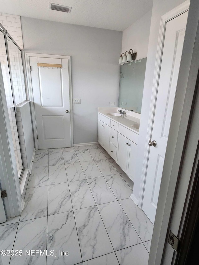 bathroom with a shower with door, vanity, and a textured ceiling