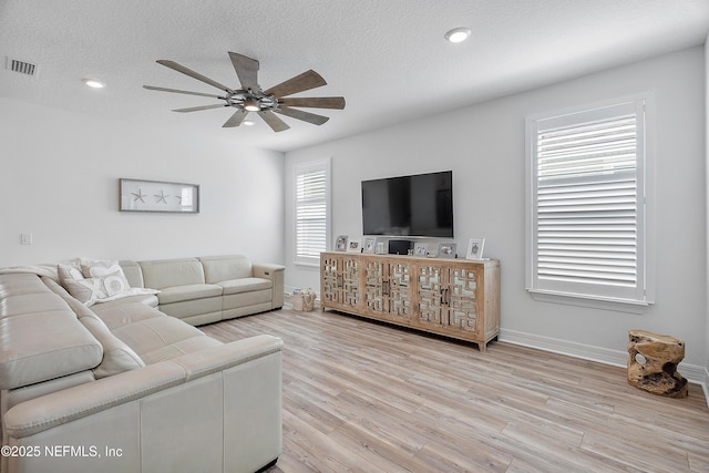 living room with ceiling fan, light hardwood / wood-style floors, and a textured ceiling