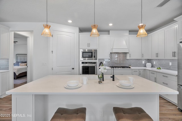 kitchen featuring stainless steel appliances, decorative light fixtures, and custom exhaust hood