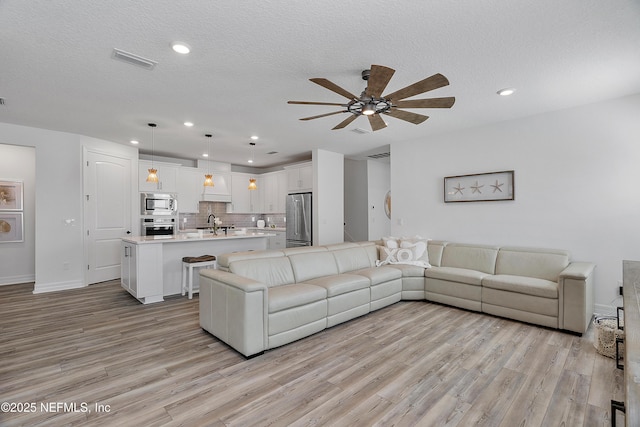 living room featuring ceiling fan, sink, a textured ceiling, and light wood-type flooring