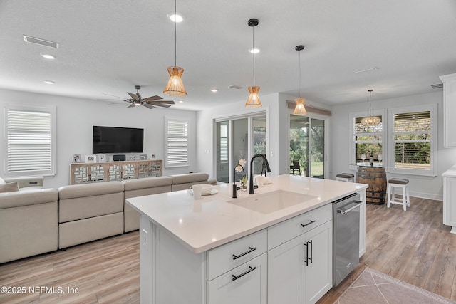 kitchen with sink, an island with sink, white cabinets, decorative light fixtures, and light wood-type flooring