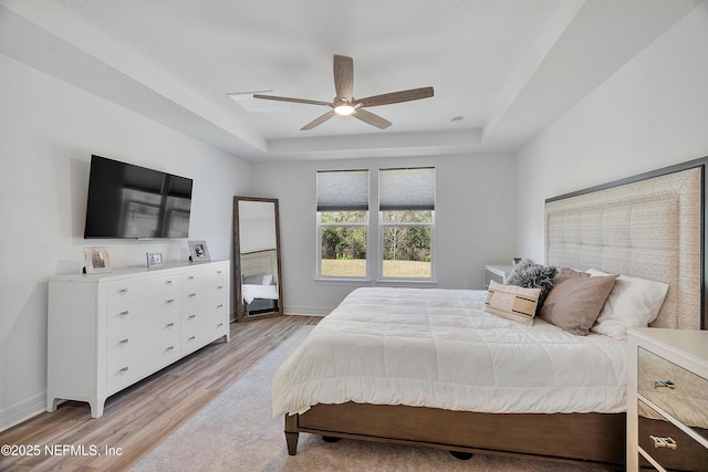 bedroom with ceiling fan, a tray ceiling, light hardwood / wood-style floors, and a textured ceiling