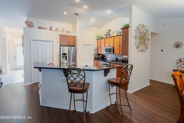 kitchen featuring appliances with stainless steel finishes, dark hardwood / wood-style floors, an island with sink, a kitchen bar, and vaulted ceiling