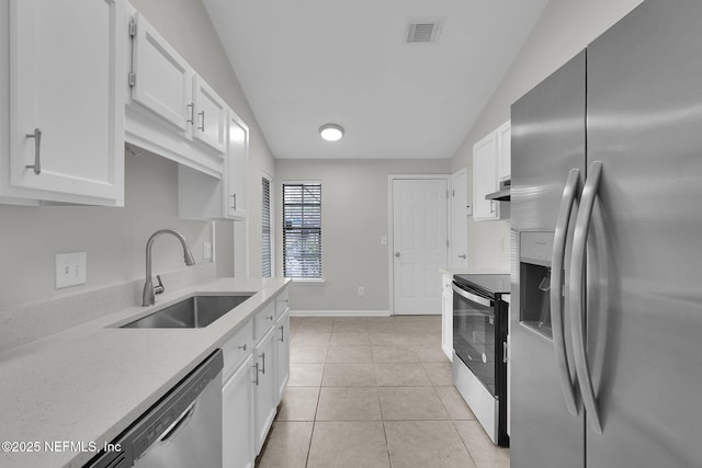 kitchen featuring lofted ceiling, sink, light tile patterned floors, appliances with stainless steel finishes, and white cabinetry