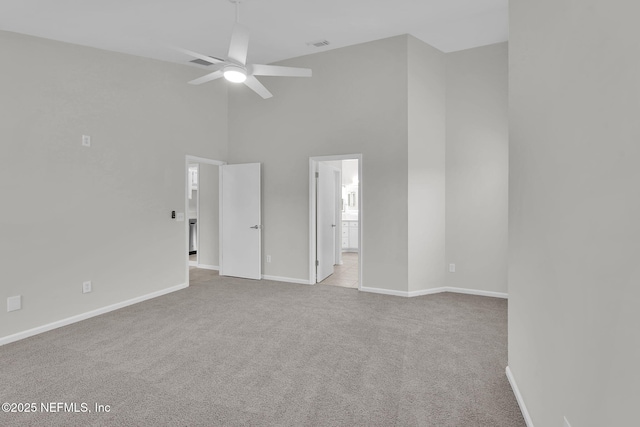 empty room featuring ceiling fan, light colored carpet, and a high ceiling