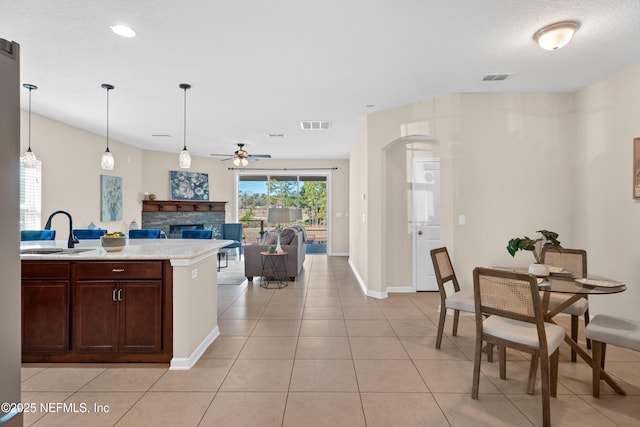 kitchen featuring dark brown cabinetry, a stone fireplace, sink, hanging light fixtures, and light tile patterned floors