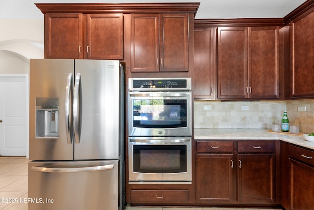 kitchen featuring light tile patterned flooring, appliances with stainless steel finishes, light stone counters, and decorative backsplash