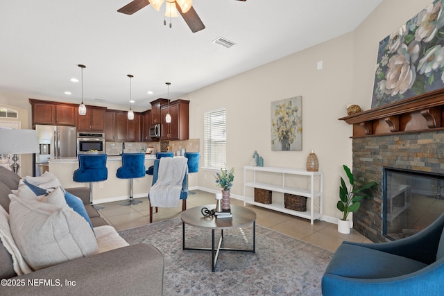 living room with a stone fireplace, ceiling fan, and light tile patterned flooring