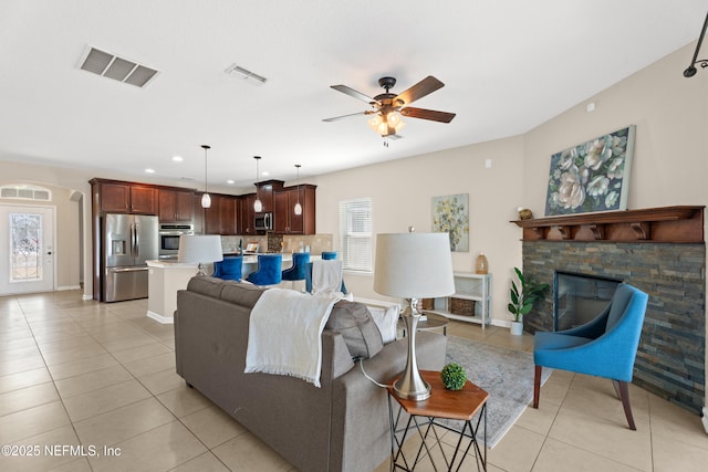 tiled living room with a stone fireplace and ceiling fan