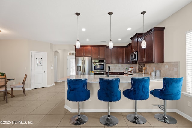 kitchen featuring sink, tasteful backsplash, light stone counters, hanging light fixtures, and stainless steel appliances