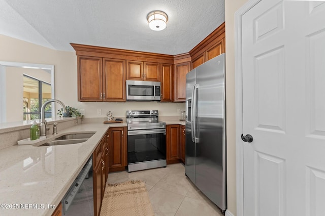 kitchen with sink, a textured ceiling, light tile patterned floors, appliances with stainless steel finishes, and light stone countertops