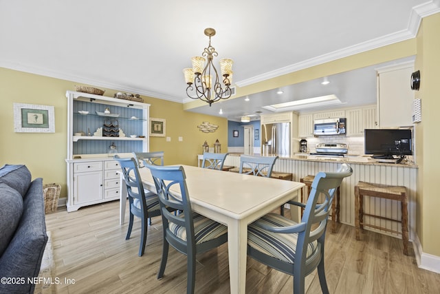 dining area with an inviting chandelier, ornamental molding, a raised ceiling, and light hardwood / wood-style flooring