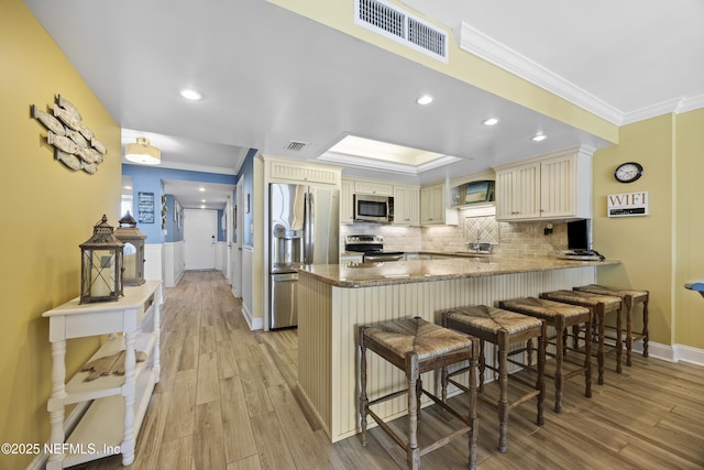 kitchen featuring a kitchen bar, kitchen peninsula, stainless steel appliances, crown molding, and light wood-type flooring