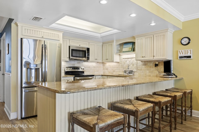 kitchen featuring stainless steel appliances, cream cabinets, a breakfast bar area, and kitchen peninsula