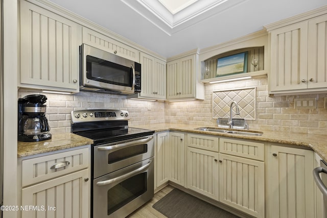 kitchen with sink, light stone counters, appliances with stainless steel finishes, cream cabinets, and backsplash