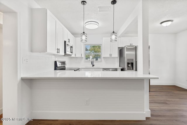 kitchen with pendant lighting, stainless steel appliances, kitchen peninsula, and white cabinets