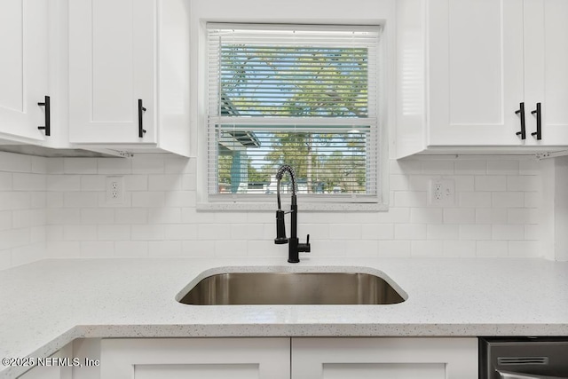 kitchen with light stone counters, white cabinetry, sink, and tasteful backsplash