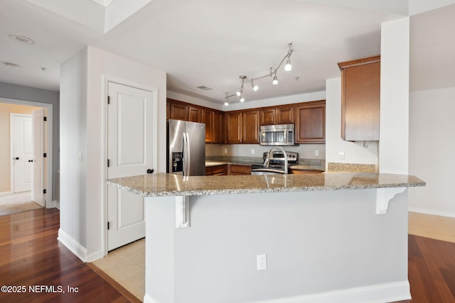 kitchen with stainless steel appliances, light stone countertops, a kitchen bar, and kitchen peninsula