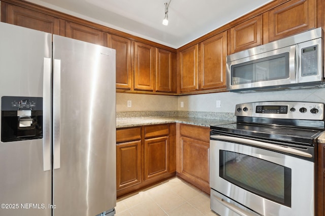 kitchen with light tile patterned flooring, stainless steel appliances, light stone countertops, and decorative backsplash