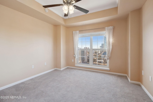 carpeted empty room featuring a raised ceiling, ornamental molding, and ceiling fan