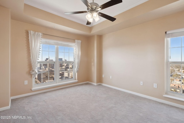 carpeted empty room featuring a raised ceiling, a wealth of natural light, and ceiling fan