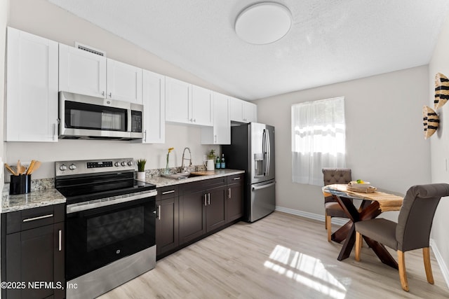 kitchen with sink, light wood-type flooring, appliances with stainless steel finishes, light stone countertops, and white cabinets