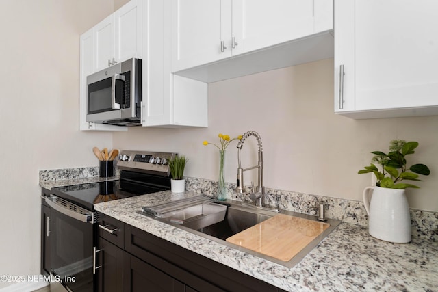 kitchen featuring stainless steel appliances, white cabinetry, sink, and light stone counters