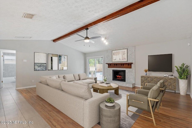 living room with a fireplace, lofted ceiling with beams, a textured ceiling, and light wood-type flooring