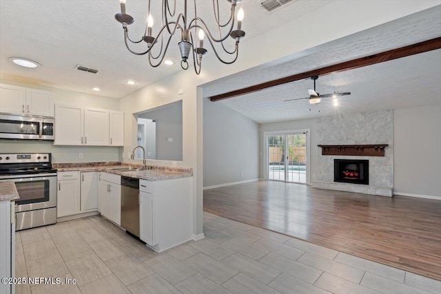 kitchen with white cabinetry, sink, a high end fireplace, stainless steel appliances, and beam ceiling