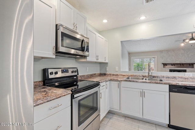 kitchen featuring appliances with stainless steel finishes, sink, white cabinets, light stone counters, and a textured ceiling