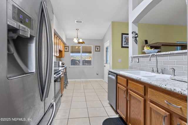 kitchen with light tile patterned flooring, sink, light stone counters, hanging light fixtures, and appliances with stainless steel finishes