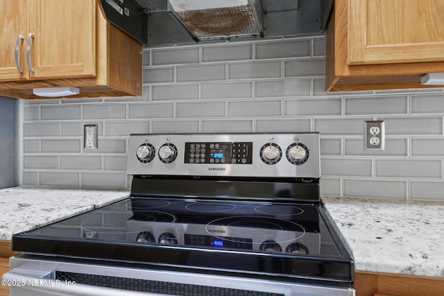 interior details featuring ventilation hood, stainless steel range with electric cooktop, light stone counters, and decorative backsplash