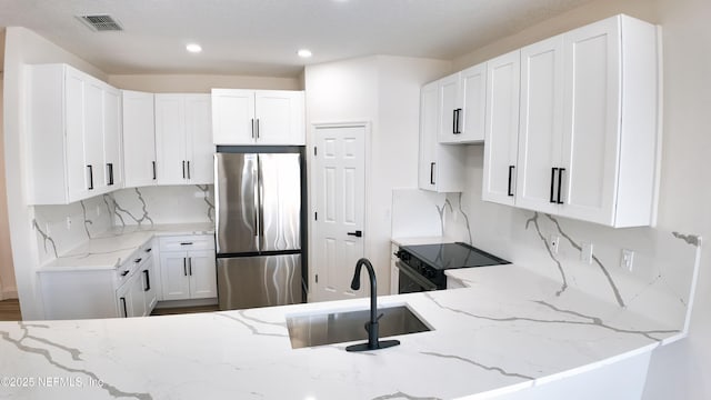 kitchen featuring sink, stainless steel fridge, black range with electric stovetop, light stone counters, and white cabinets