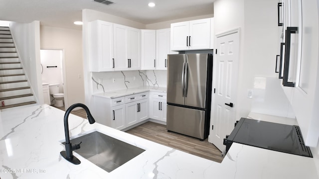 kitchen featuring sink, stainless steel fridge, white cabinetry, light stone countertops, and decorative backsplash