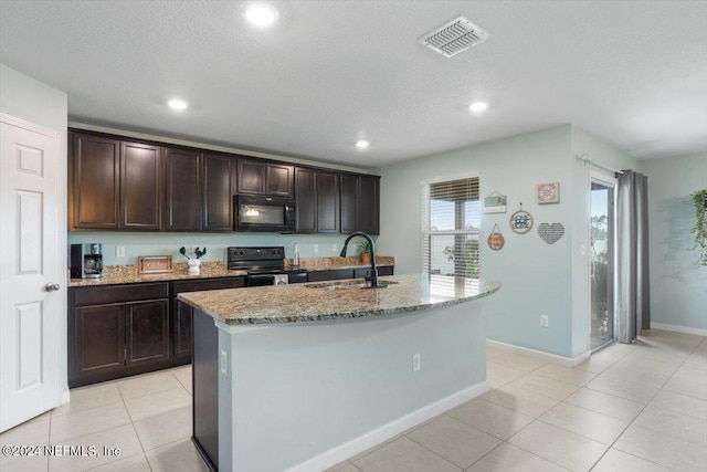 kitchen featuring sink, a kitchen island with sink, light stone counters, dark brown cabinetry, and black appliances