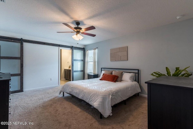 bedroom with connected bathroom, carpet, ceiling fan, a barn door, and a textured ceiling