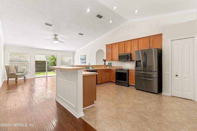 kitchen with vaulted ceiling, appliances with stainless steel finishes, kitchen peninsula, ceiling fan, and light hardwood / wood-style floors