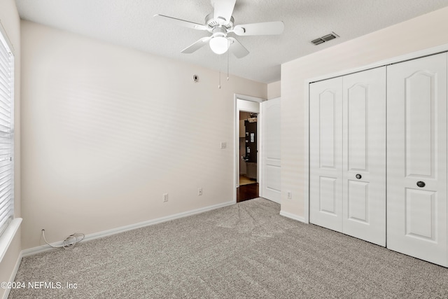 unfurnished bedroom featuring ceiling fan, light colored carpet, a closet, and a textured ceiling