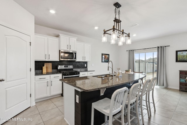 kitchen featuring sink, a center island with sink, dark stone countertops, stainless steel appliances, and white cabinets